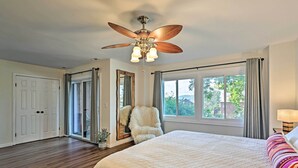 Une chambre avec un grand lit, un ventilateur de plafond, une fenêtre avec des rideaux et une porte.