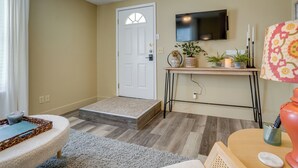 A living room with a sofa, a coffee table, a TV mounted on the wall, a door, and a small console table with decorative items. - Kerrville Vacation Rental Across From River Trail! (Kerrville)