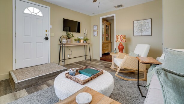 A living room with a white door, a ceiling fan, a TV, a wooden desk, a rocking chair, and a white couch. - Kerrville Vacation Rental Across From River Trail! (Kerrville)