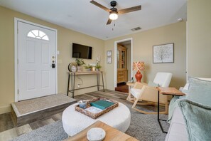 A living room with a white door, a ceiling fan, a TV, a wooden desk, a rocking chair, and a white couch. - Kerrville Vacation Rental Across From River Trail! (Kerrville)