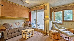 Un salón acogedor con sofá, una mesa de centro, una silla y un amplio ventanal con vistas al exterior.