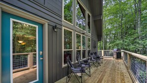 Une terrasse couverte avec des sièges d’extérieur et un barbecue, entourée d’une terrasse en bois et d’une rambarde en métal.