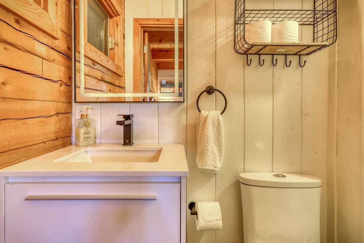 Un baño con pared de madera, un lavabo blanco, un espejo, un inodoro y un perchero con toallas.