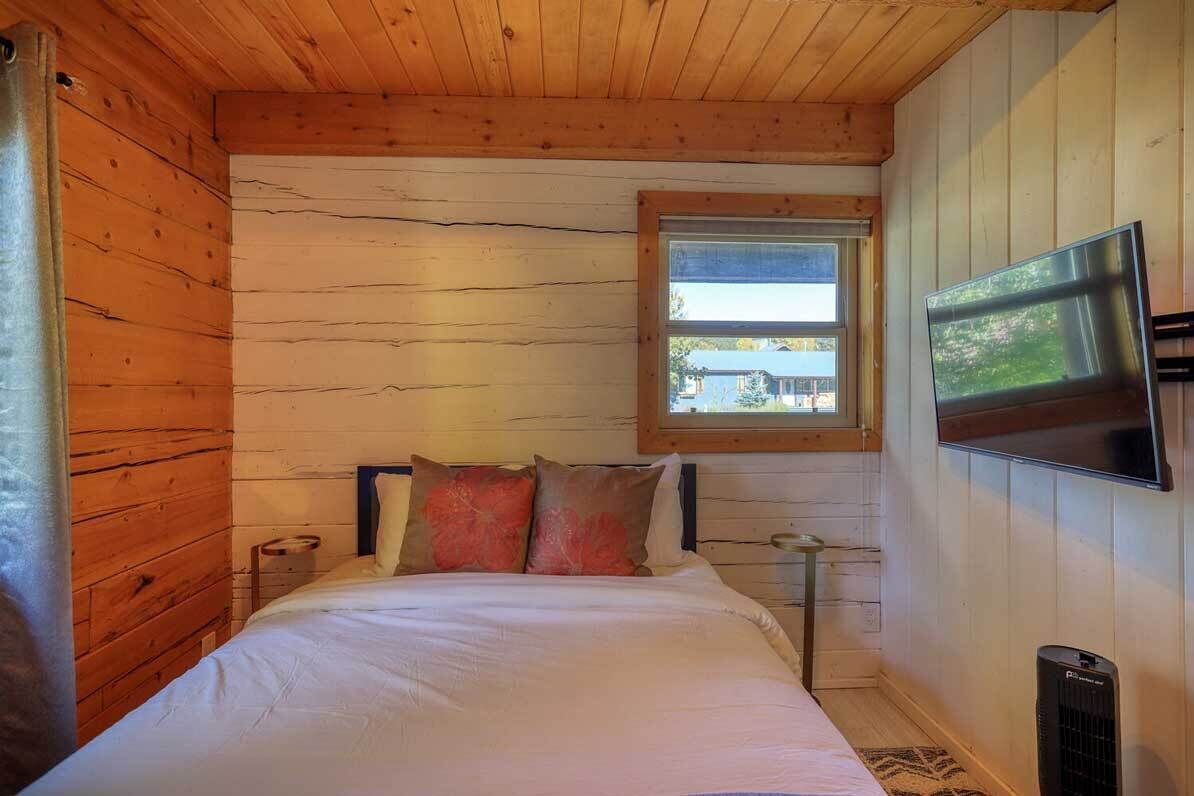 Ein Zimmer in einer Holzhütte mit einem Bett, einem Fenster, einem Fernseher und einer Heizung.