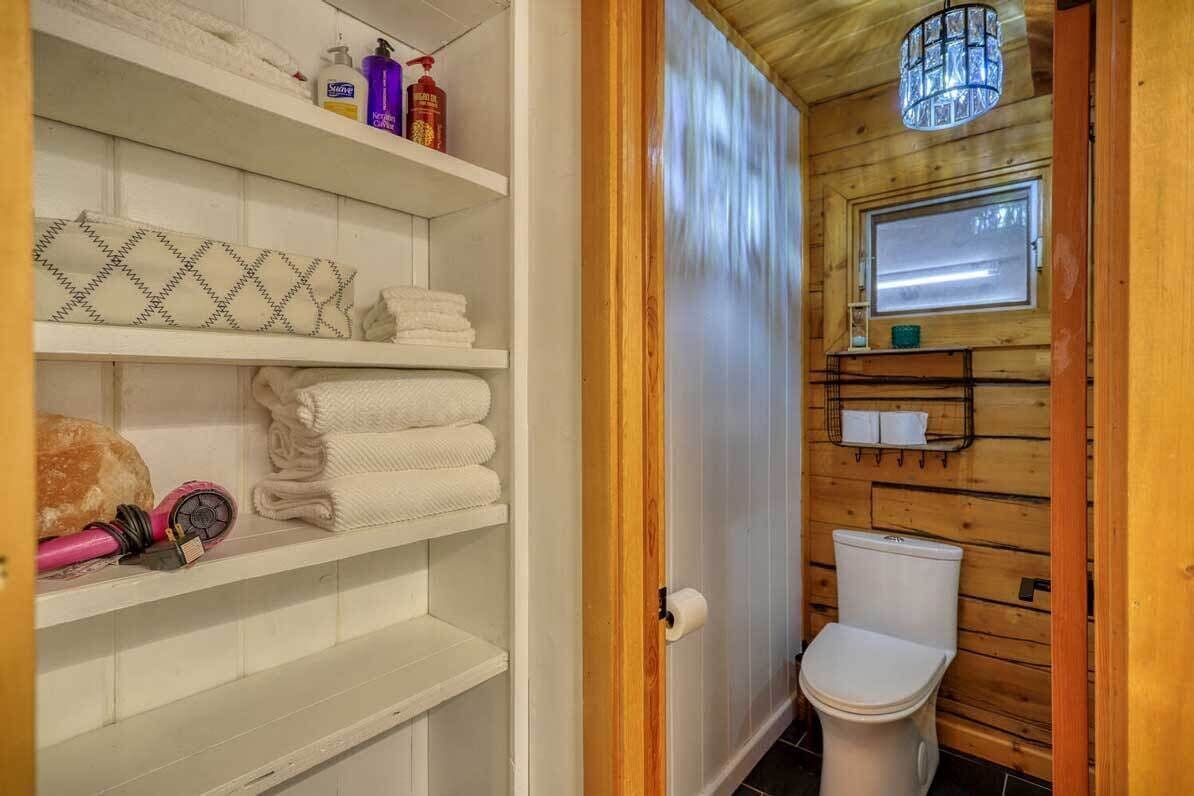 A wooden interior with a toilet, shelves with towels, and toiletries.