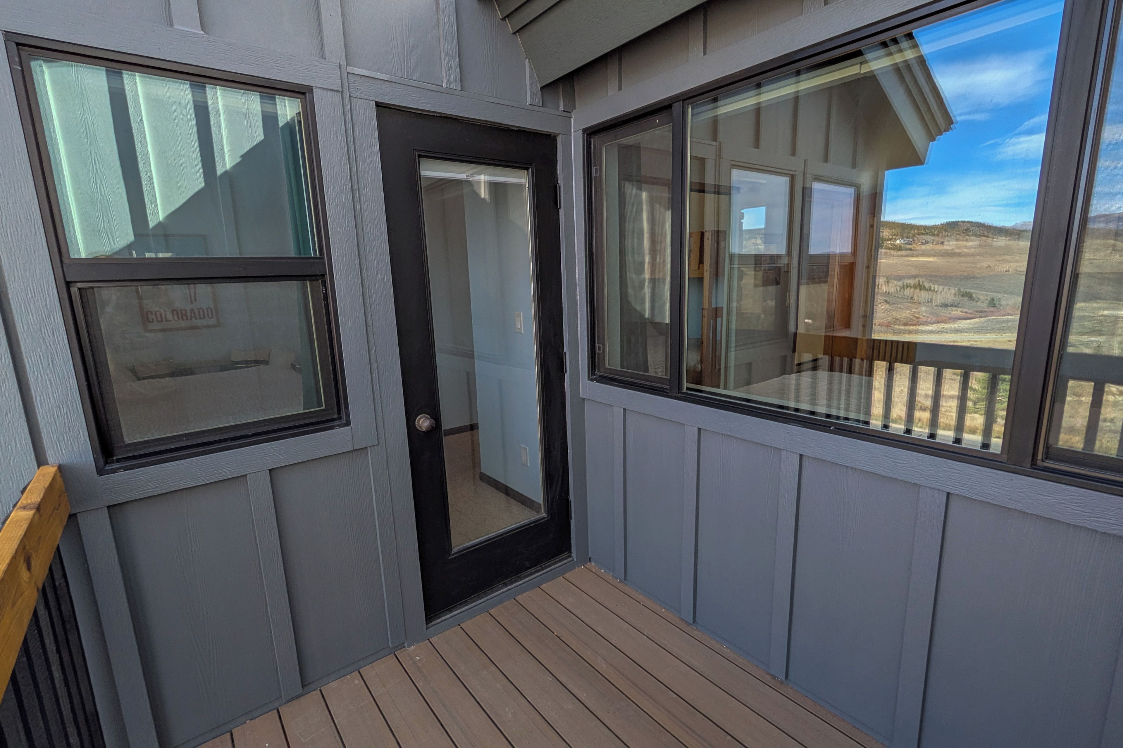A balcony with a wooden floor, a door, and two windows.