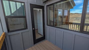 A balcony with a wooden floor, a door, and two windows.