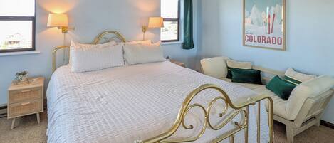 A bedroom with a bed, bedside tables, a sofa, and a wall-mounted lamp.