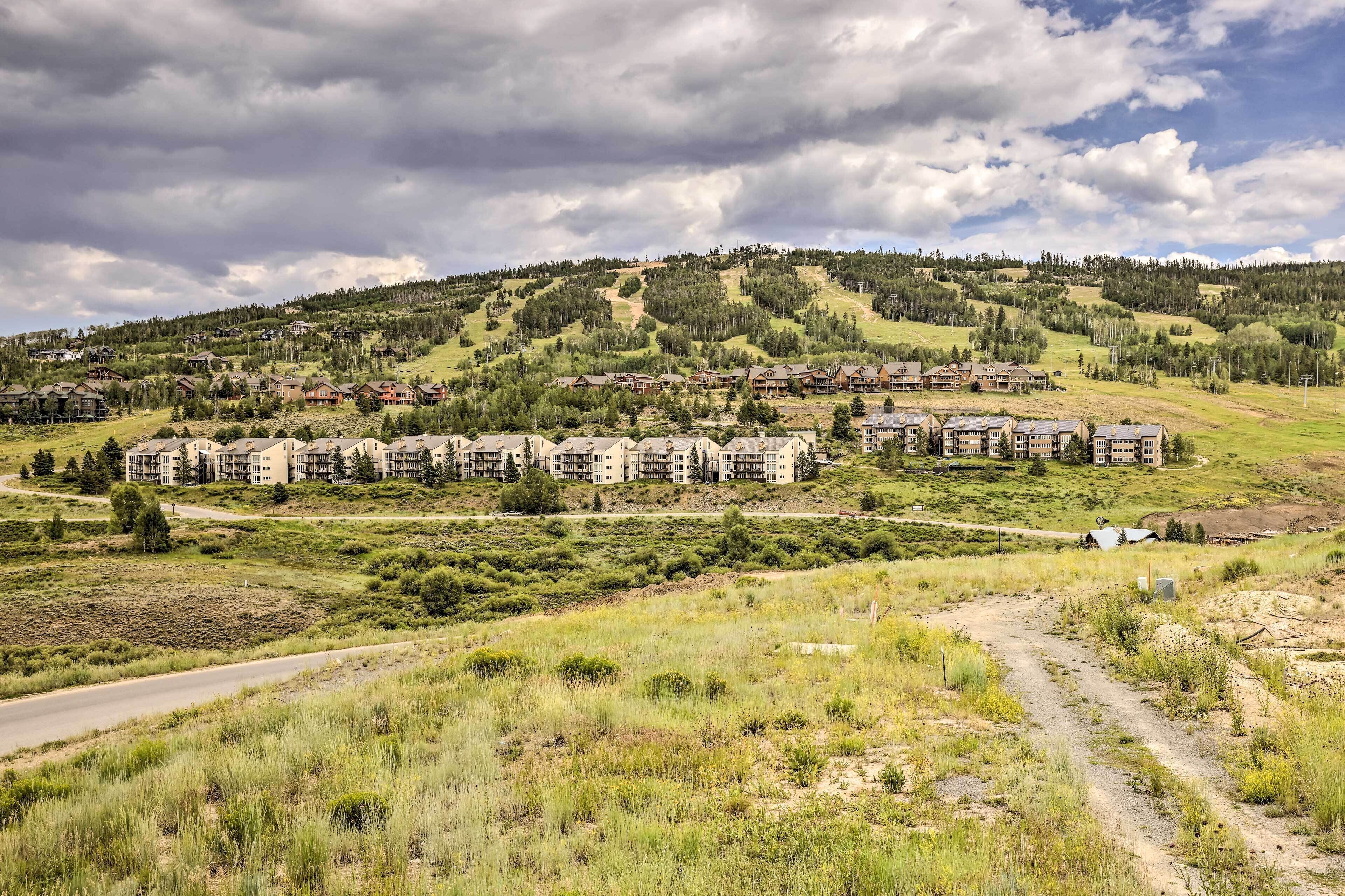 A residential area with multiple apartment buildings, a winding road, and a hilly landscape with trees.