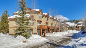 A snow-covered road leading to a row of multi-story buildings with balconies, surrounded by trees and snowbanks. - Airy Winter Park Gem w/ Private Outdoor Hot Tub! (Winter Park)