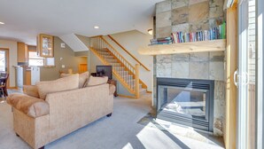 A living room with a beige sofa, a fireplace, a staircase, and a bookshelf. - Airy Winter Park Gem w/ Private Outdoor Hot Tub! (Winter Park)