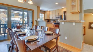 A dining area with a large table set for six, kitchen cabinets, a microwave, and a view through large windows. - Airy Winter Park Gem w/ Private Outdoor Hot Tub! (Winter Park)