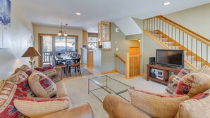 A spacious living room with a sofa set, a glass coffee table, and a television on a wooden stand. A staircase with a wooden railing leads to an upper level. - Airy Winter Park Gem w/ Private Outdoor Hot Tub! (Winter Park)