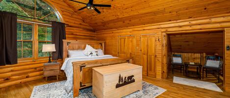 A log cabin bedroom with a bed, nightstand, dresser, and a large window with curtains.