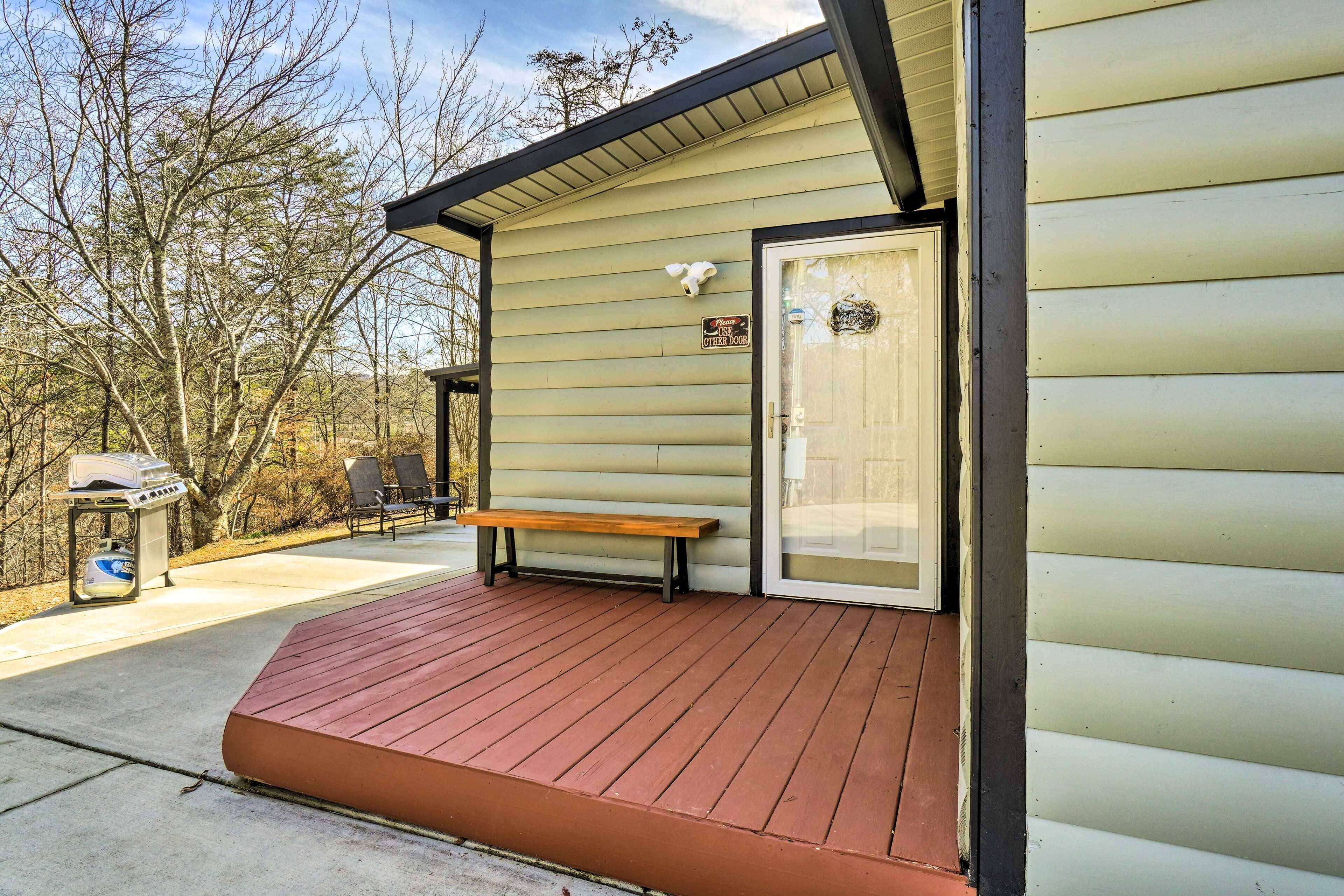A wooden deck with a bench, a grill, and a door to a building.