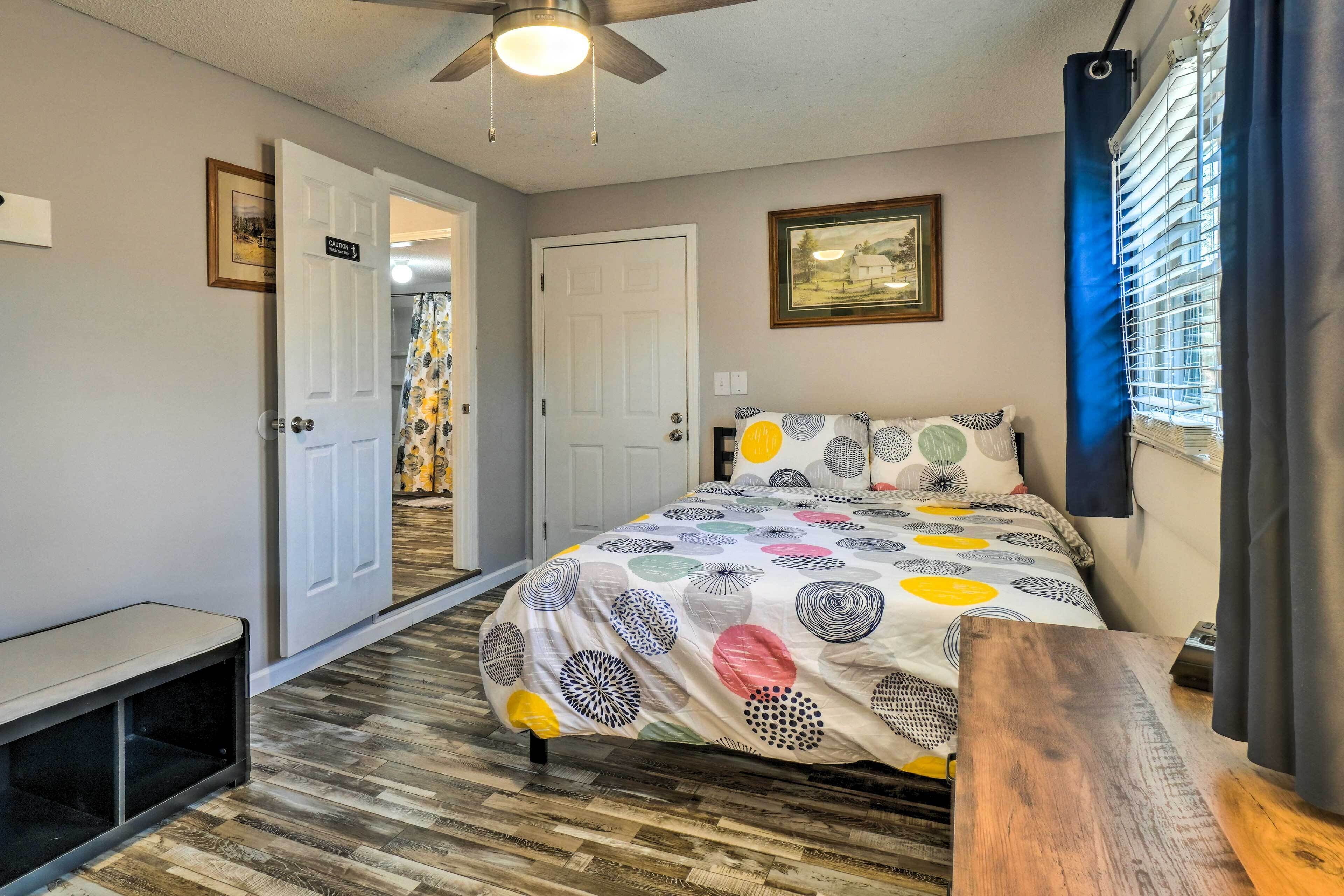 A bedroom with a bed, a bench, a ceiling fan, and a door leading to another room.
