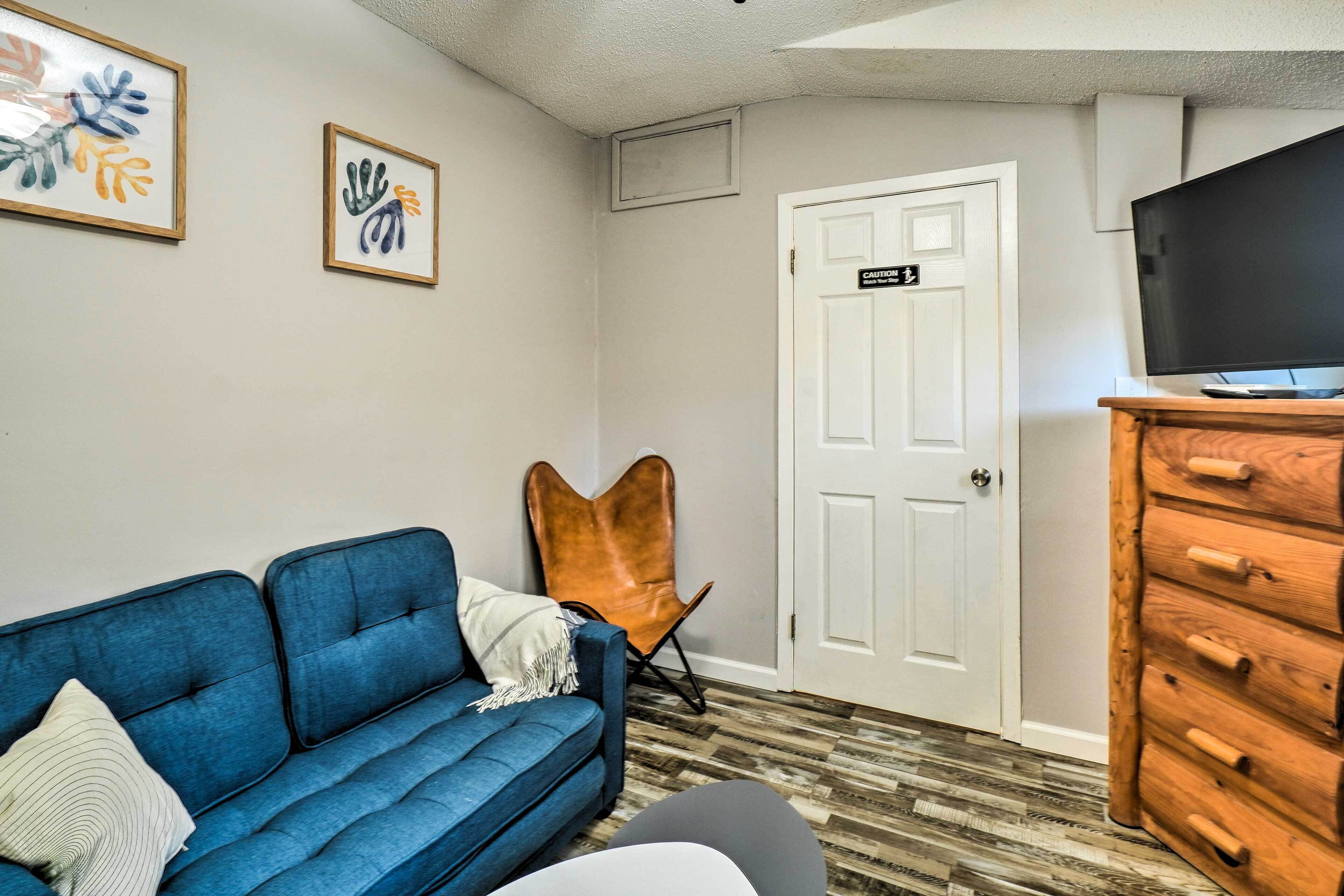 A room with a blue sofa, a wooden dresser, a television, and two framed artworks on the wall.