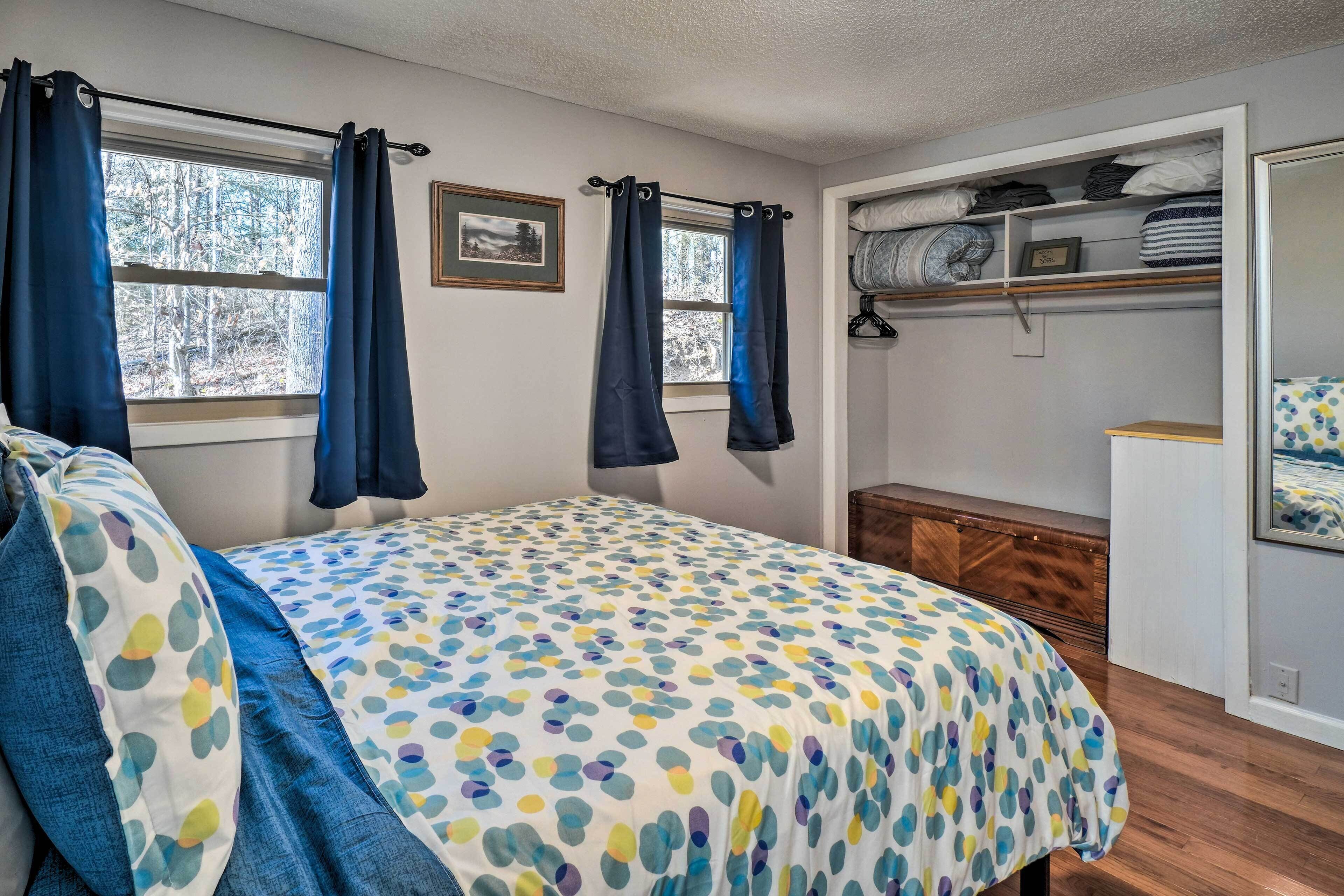 A bedroom with a bed, a window with curtains, a bedside table, a wardrobe, and a shelf with folded items.