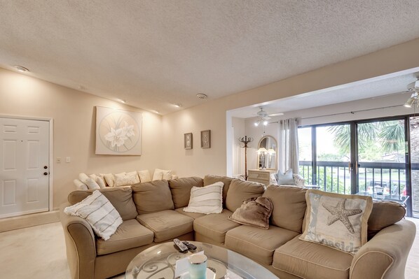 A living room with a beige sectional sofa, a coffee table, and a large window with a view of greenery.