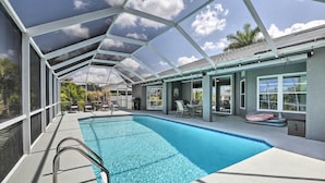 A covered swimming pool with a clear blue water, surrounded by lounge chairs and tables, under a transparent roof structure. - Private Pool & Canal Views: Home in Cape Coral (Cape Coral)