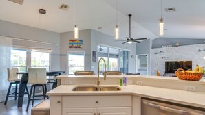 A modern kitchen with a central island, a dining area with bar stools, and a view of the outdoors. - Private Pool & Canal Views: Home in Cape Coral (Cape Coral)