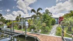 A wooden dock leading to a house with a garden and a pond. - Private Pool & Canal Views: Home in Cape Coral (Cape Coral)