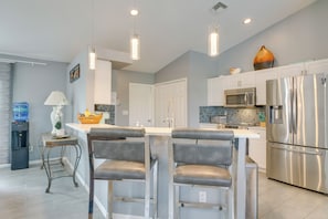 A modern kitchen with stainless steel appliances, a white island with bar stools, and pendant lighting.