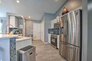 A modern kitchen with stainless steel appliances, a tiled backsplash, and a light blue wall.