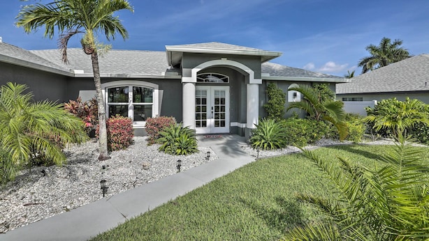 A modern house with a well-maintained lawn, palm trees, and a clear sky. - Private Pool & Canal Views: Home in Cape Coral (Cape Coral)