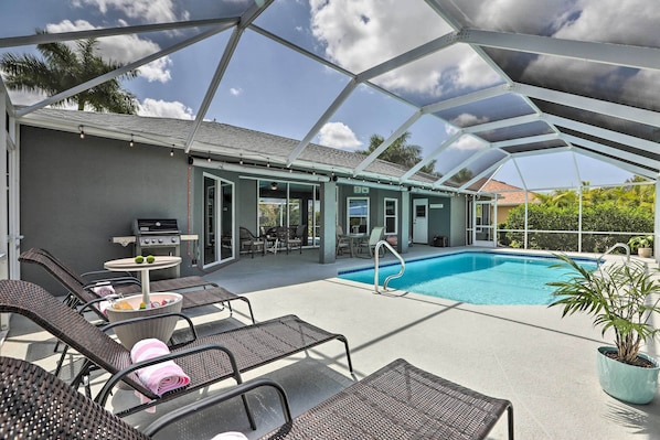 An outdoor pool area with lounge chairs and a grill.