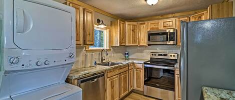 A compact kitchen with wooden cabinets, a stainless steel refrigerator, a dishwasher, a microwave, and an oven.