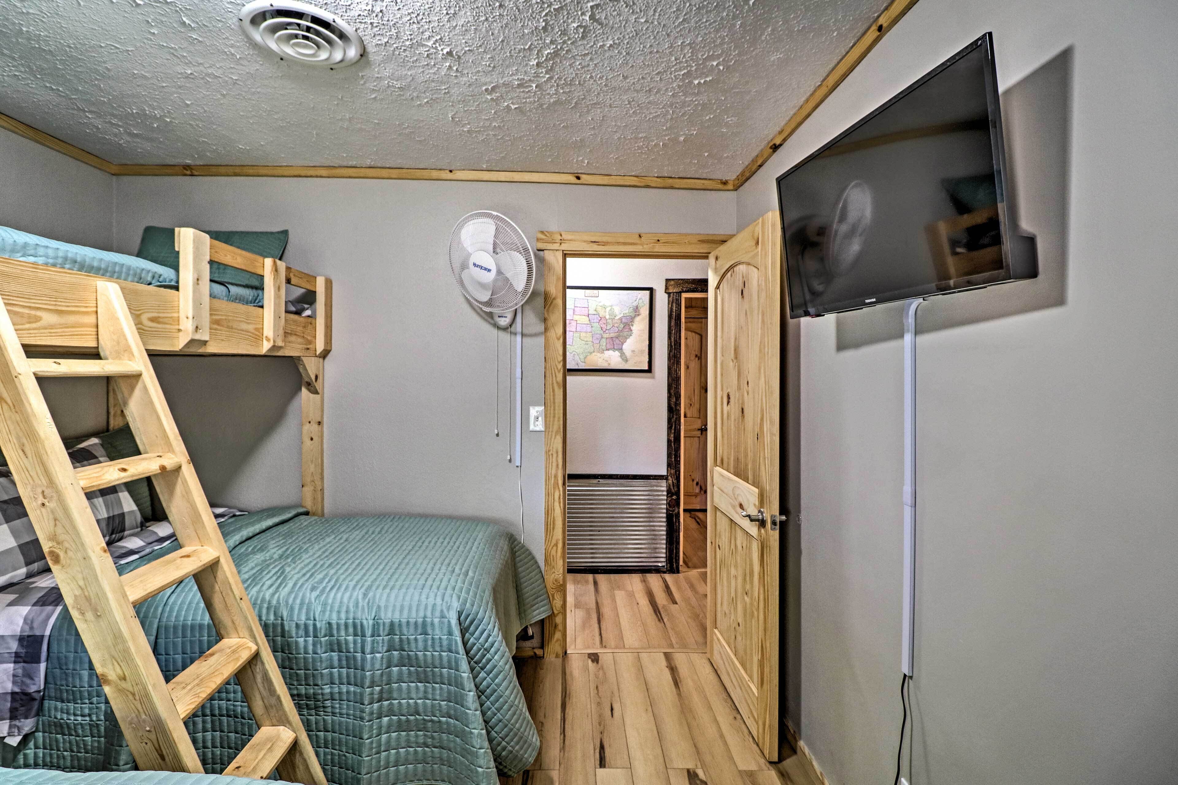 A compact room with bunk beds, a fan, a TV, and a door leading to another room.