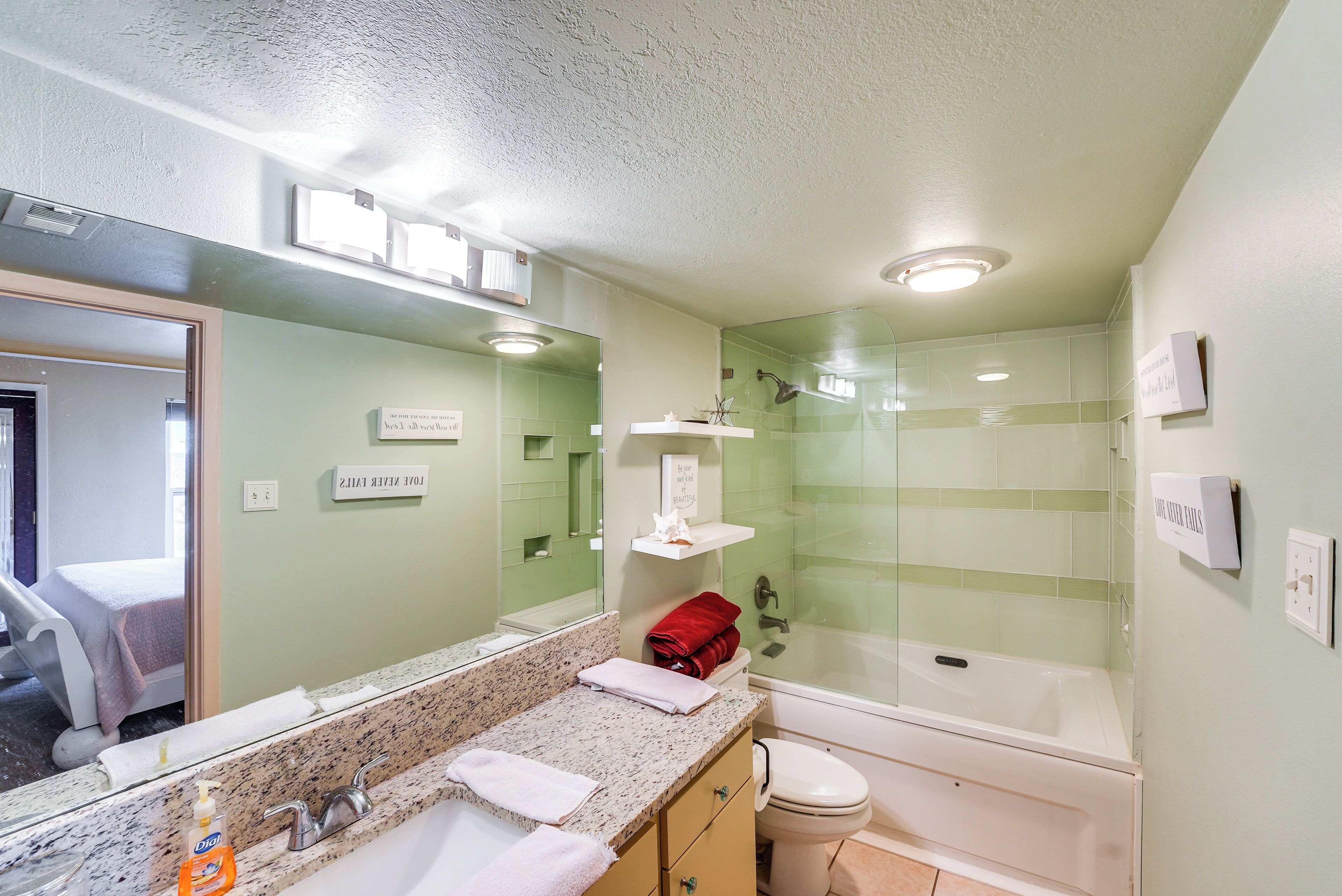 A bathroom with a granite countertop, a white toilet, a glass-enclosed shower, and a mirror with a sign above it.