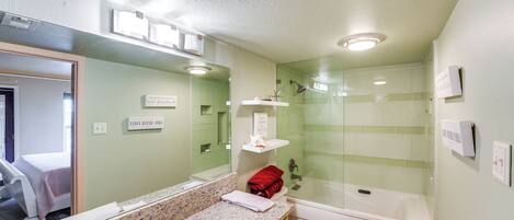 A bathroom with a granite countertop, a white toilet, a glass-enclosed shower, and a mirror with a sign above it.