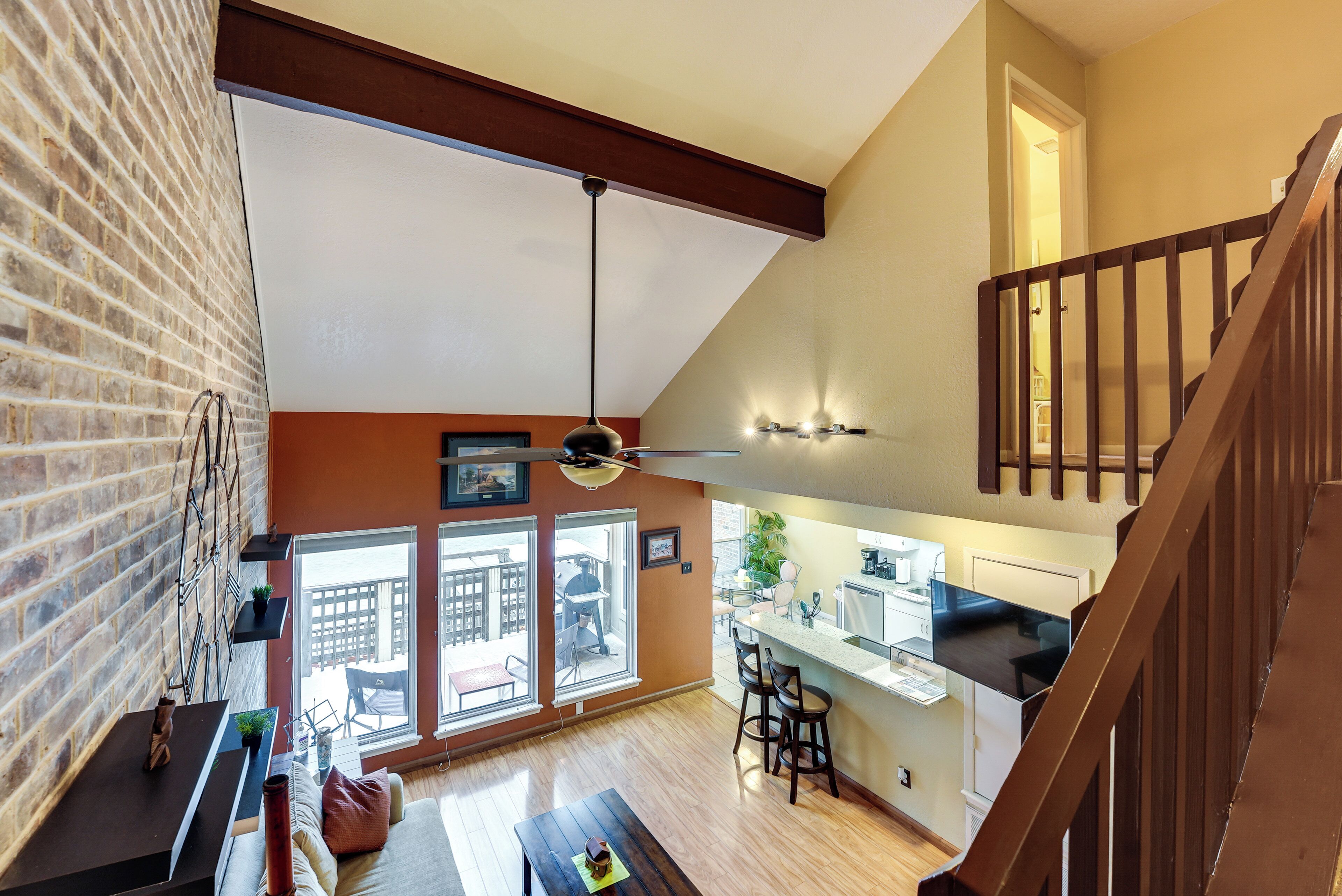 A spacious loft with a high ceiling, exposed brick walls, a kitchen area, and a view to the outside.