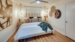 Ein Schlafzimmer mit einem Bett, einem Deckenventilator, Nachttischen, Wandbildern und einer Tür.