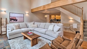 A spacious living room with a large sectional sofa, a wooden coffee table, and a fluffy rug. A staircase with wooden railings leads to an upper level. - 2 Mi to Dtwn: Leadville Haven w/ 2 Furnished Decks (Leadville)