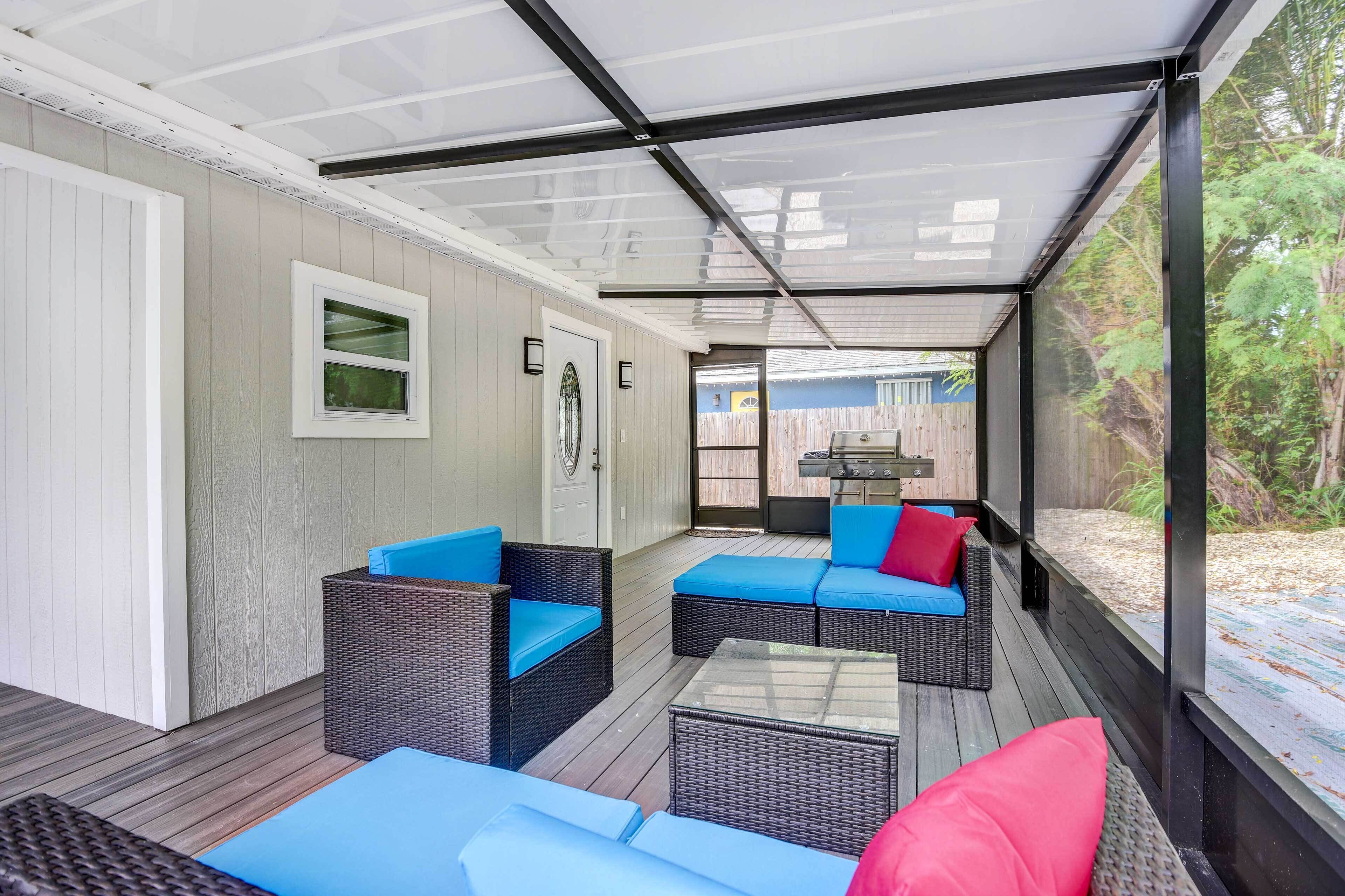 A covered outdoor area with wicker furniture and a glass ceiling, leading to a backyard with a barbecue grill.