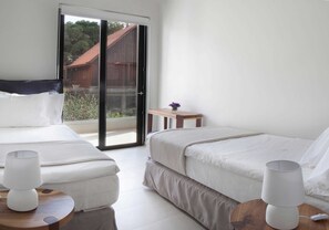 A hotel room with two beds, a small table, a lamp, and a view of the outside.