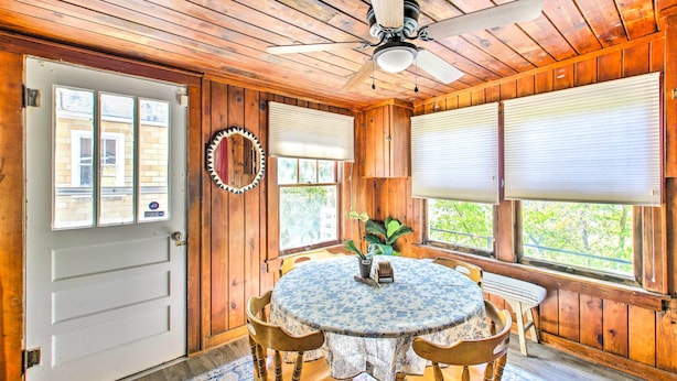 Un intérieur en bois avec une table ronde, des chaises, un ventilateur de plafond et des fenêtres équipées de stores.