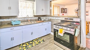 Une cuisine compacte avec des meubles blancs, un four à micro-ondes encastré, une cuisinière et une fenêtre agrémentée d’un paravent décoratif.