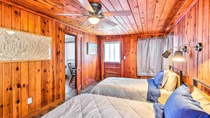 Une chambre dans un chalet en bois, avec deux lits, un ventilateur de plafond et une fenêtre avec des rideaux.
