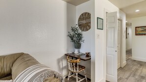 A hallway with a white door, a wooden floor, a beige sofa, a wicker chair, and a wall clock. - South Padre Island Getaway - Newly Renovated! (South Padre Island)