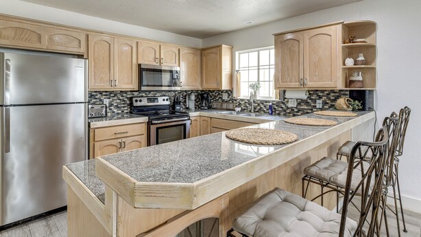 A modern kitchen with granite countertops, stainless steel appliances, wooden cabinets, and a bar area with stools. - South Padre Island Getaway - Newly Renovated! (South Padre Island)