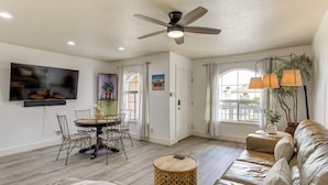 A living room with a ceiling fan, a flat-screen TV, a dining table with chairs, a sofa, and a round wooden stool. - South Padre Island Getaway - Newly Renovated! (South Padre Island)