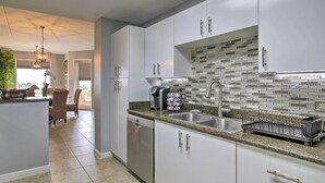 A modern kitchen with white cabinets, a granite countertop, a dishwasher, a sink, and a backsplash with mosaic tiles. - Sunny SPI Las Villas Condo w/ Resort Amenities! (South Padre Island)