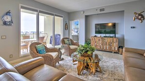 A living room with leather sofas, wicker chairs, a glass coffee table, and a large flat-screen TV. - Sunny SPI Las Villas Condo w/ Resort Amenities! (South Padre Island)