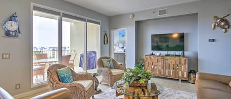 A living room with leather sofas, wicker chairs, a glass coffee table, and a large flat-screen TV.