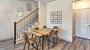 Un comedor con una mesa y sillas de madera, una escalera con barandilla de metal y una puerta con interruptor de luz.