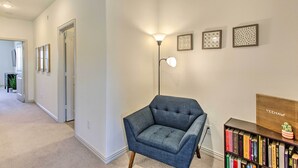 Un pasillo con un sillón azul, una lámpara de pie y una estantería llena de libros.